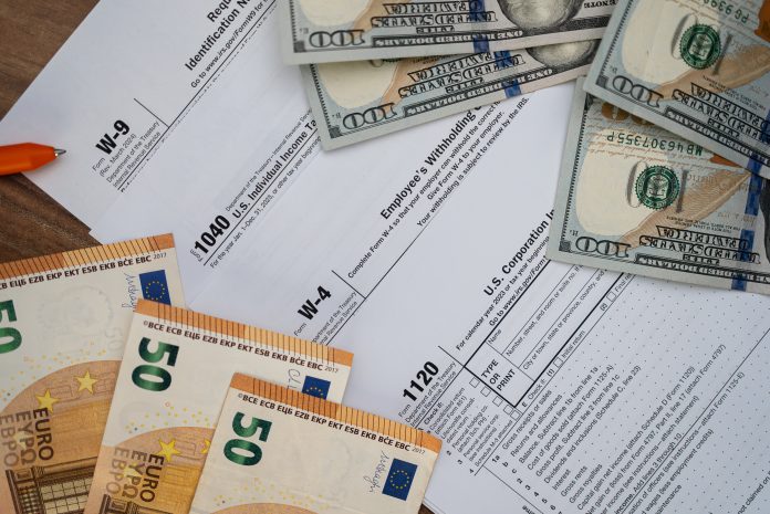 Tax forms and currency on a wooden desk, featuring U.S. dollars and euros. Financial paperwork for tax filing season. Concept of tax preparation, accounting, and financial management.