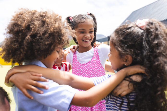 In school, diverse group of young students hugging, laughing outside. They wear casual clothes, have curly hair, and look happy, unaltered