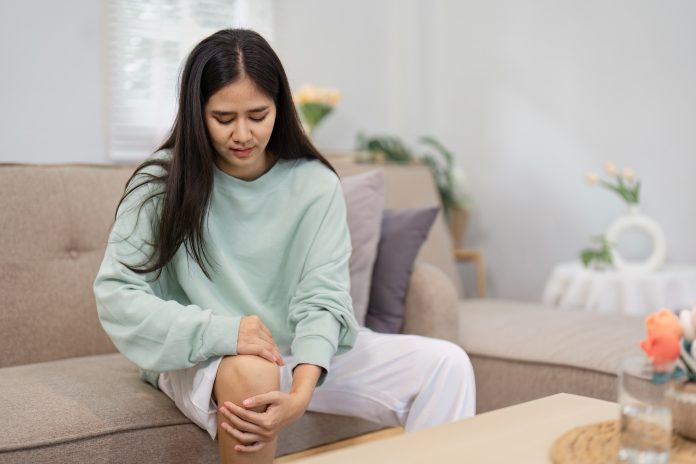 Young woman experiencing knee pain while sitting on a couch, emphasizing health awareness and self-care.